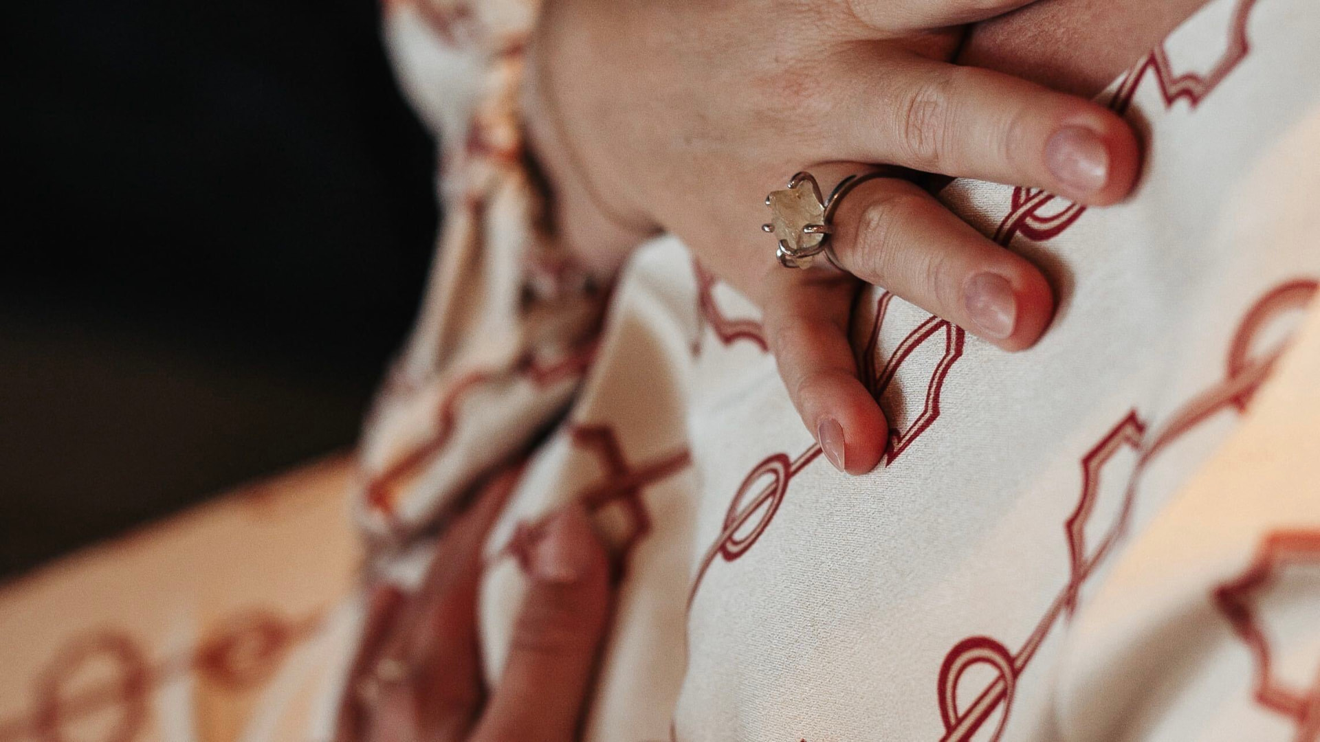 Amandas hand med ring vilande mot bröstet i ett mönstrat tyg